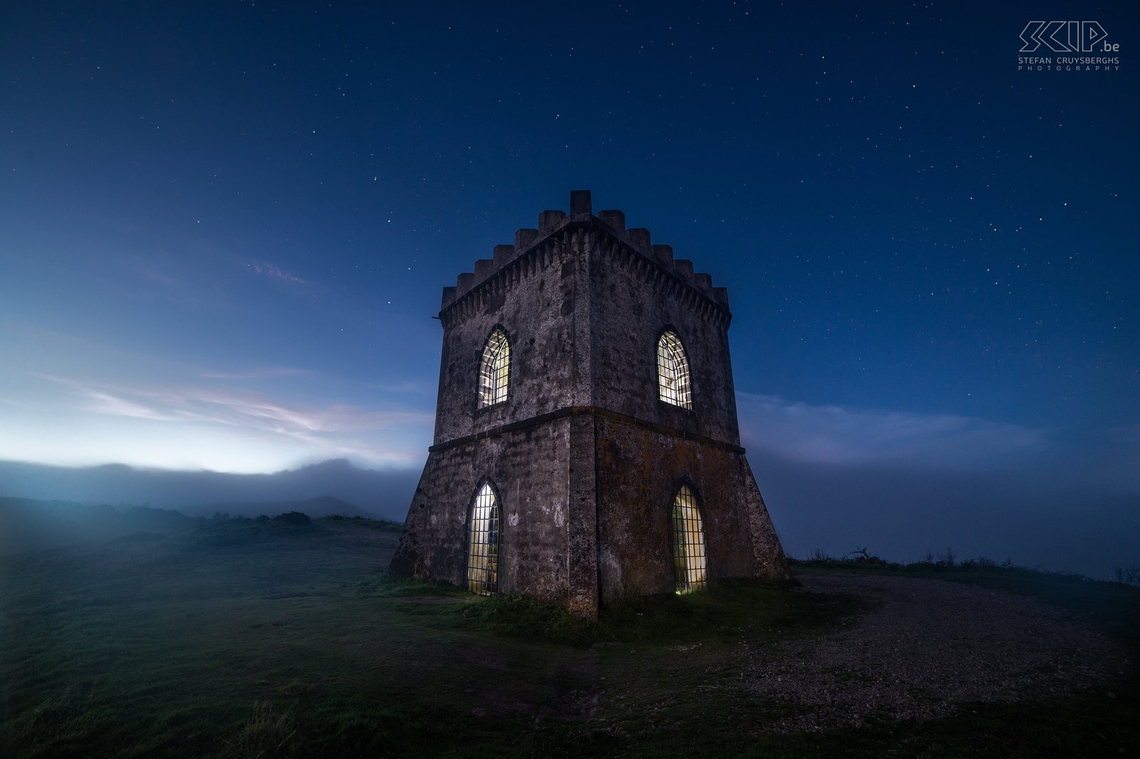 Castelo Branco by night The tower of the Castelo Branco at the end of the blue hour with some fog at the high hilltop. The Miradouro do Castelo Branco is a viewpoint at the main island São Miguel of the Azores. From there you can see the village of Villa Franca do Compo, the Furnas Lake and the Atlantic Ocean. The tower looks like a medieval fortress but it is more recent and constructed with concrete. I used some flash lights to illuminate  the insides of the tower. Stefan Cruysberghs